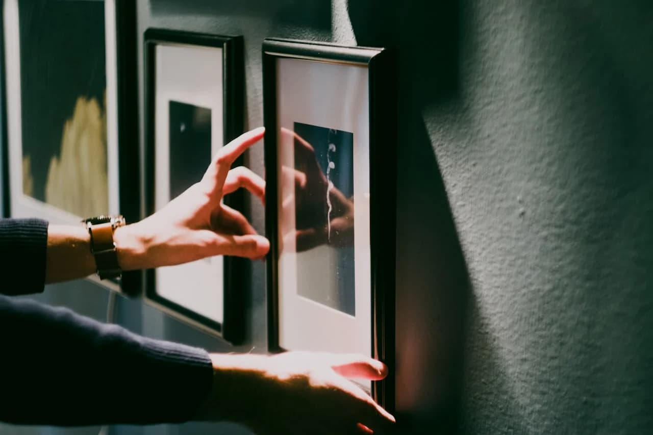 Mladá osoba ukladá štvorcové fotografie do symetrickej mriežky na stene