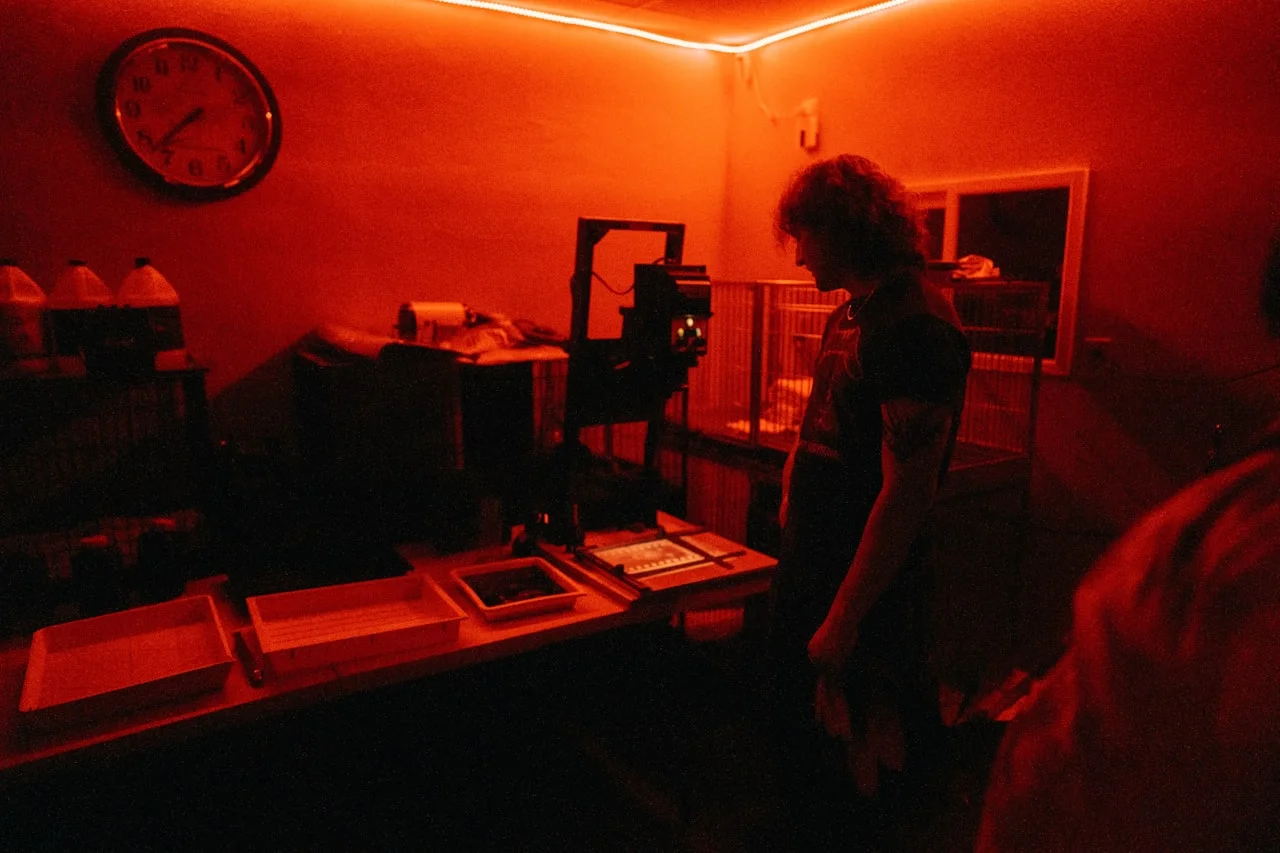 Fotograf v tmavej komore pod červeným svetlom pri spracovaní fotografie
