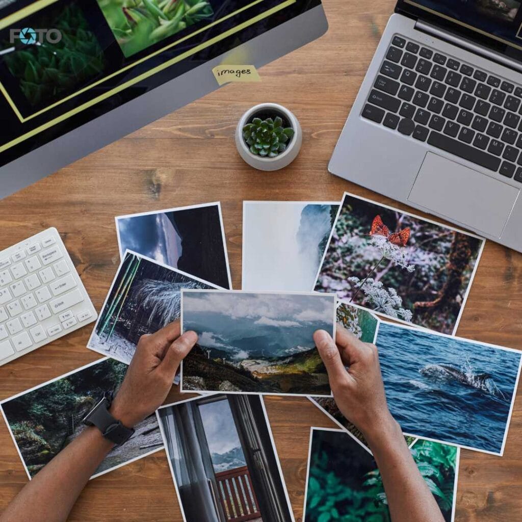 Delovni prostor z natisnjenimi fotografijami narave razporejenimi po mizi z računalnikoma